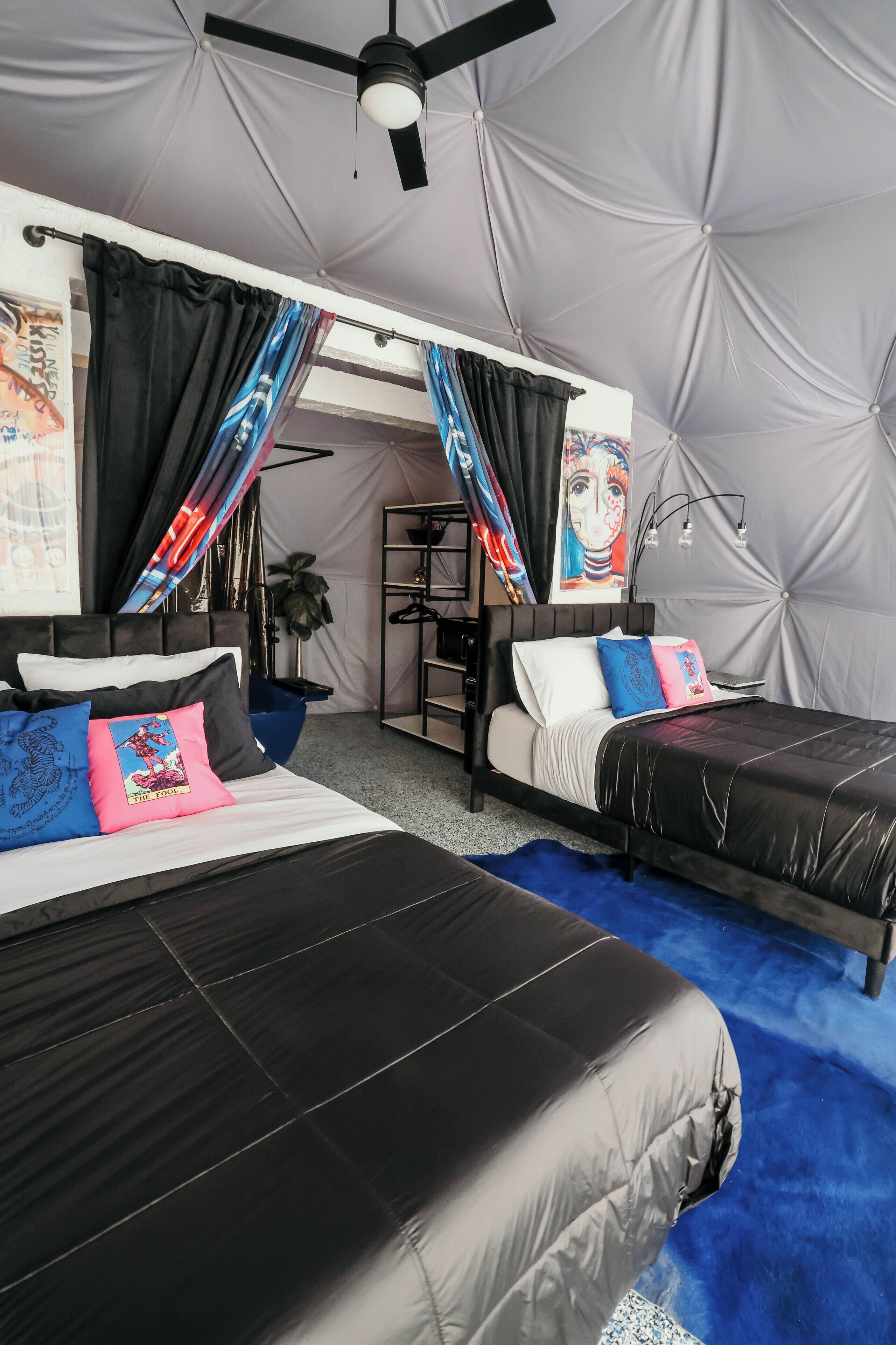 A bedroom with two beds, a ceiling fan, and a large window with curtains.