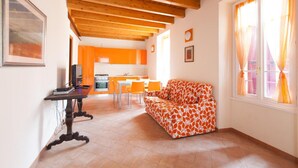 A spacious living area with a wooden ceiling, a sofa with a leaf pattern, a dining table with chairs, and a kitchen in the background. - Barchi Resort - Apartments Suites - Villa Venezia - Master Villa Venezia (San Felice del Benaco)
