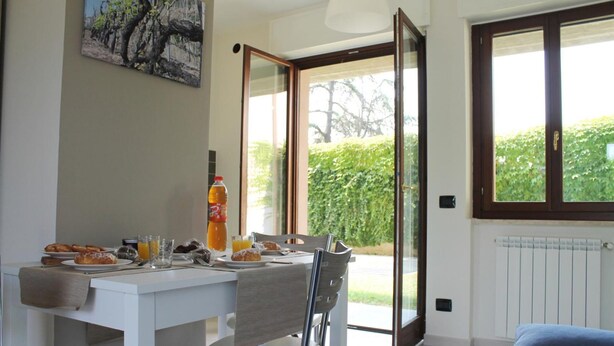 A dining area with a table set for breakfast, a painting on the wall, and a view of greenery outside. - Case Cosi Verona - Appartamento 1-4 (Verona)