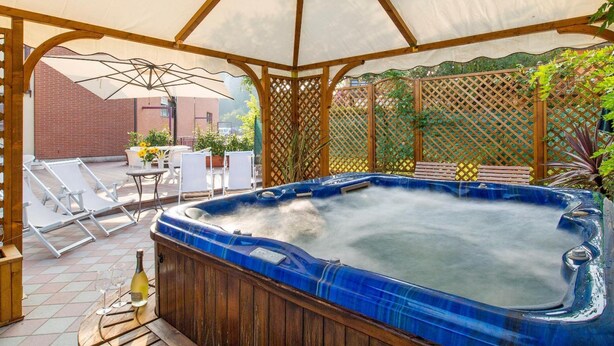 Un jacuzzi bajo una pérgola de madera con toldo blanco, rodeado de sillones de descanso y una mesa con una botella y vasos.