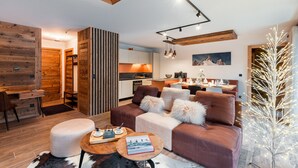 A modern living room with a sofa, ottoman, and coffee table, a kitchen in the background, and a wooden ceiling. - Thom's apartment - LES GETS: right in the center and at the foot of the slopes (Les Gets)
