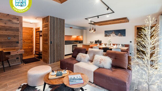 A modern interior with a wooden ceiling, a cozy seating area with a sofa and ottoman, a dining table, and a kitchen in the background. - Thom's apartment - LES GETS: right in the center and at the foot of the slopes (Les Gets)