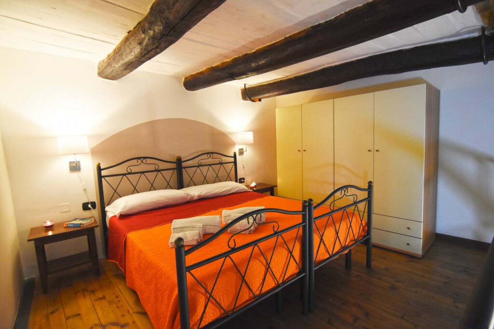 Ein Schlafzimmer mit Bett, Nachttischen, einem Kleiderschrank und freiliegenden Holzbalken.