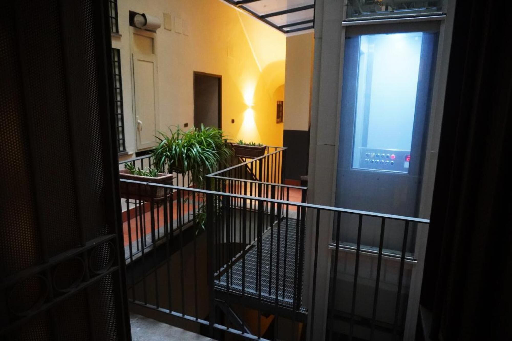 A staircase with a metal railing leading to an elevator. There are potted plants on the landing.
