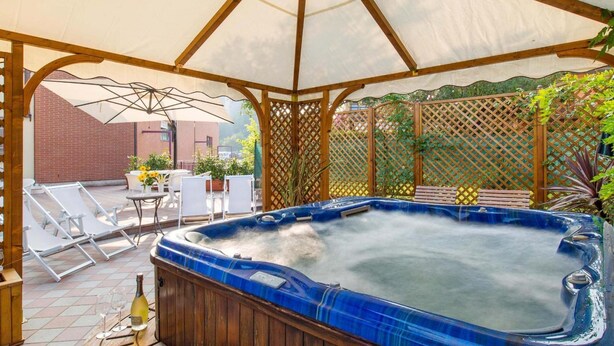 Een hottub in een overdekte buitenruimte, met lounge stoelen en een tafel met een fles en glazen.