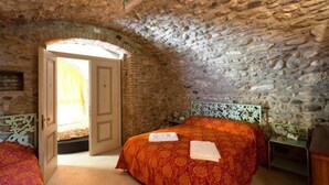 Een slaapkamer met een stenen plafond, een bed met een geborduurde spreideken en een deur naar een andere kamer.