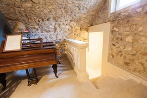 A room with a stone wall, a wooden piano, a fireplace, and a staircase. - Barchi Resort - Apartments Suites - Villa Venezia - Garden Villa Venezia (San Felice del Benaco)