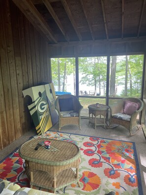 Relax in a cozy cabin-style room with a large window offering a view of the surrounding landscape, wicker furniture, and a flat-screen TV.