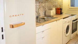 Une cuisine compacte équipée d’un réfrigérateur blanc, d’un four à micro-ondes, d’un grille-pain, d’un lave-linge et d’un évier.