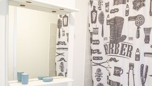 Une salle de bain avec un lavabo blanc, un miroir et un rideau de douche orné d’illustrations représentant un salon de coiffure.