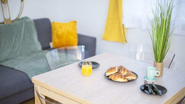 Un salon moderne avec une table basse en bois, une table à manger en verre et un canapé agrémenté de coussins.