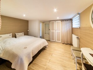 Een slaapkamer met een groot bed, een nachtkastje, een stoel, een radiator en een deur naar een balkon.
