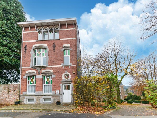 Een gebouw van rode baksteen met een witte deur en ramen, omringd door bomen en een heldere lucht.