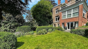A well-maintained garden with a lawn and hedges, a brick house with large windows, and a clear blue sky. - Holiday Home With Character in Stavelot (Stavelot)