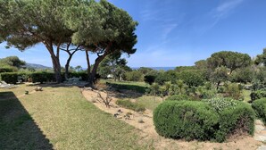 Un jardín con mesa y sillas, rodeado de árboles y vistas al mar.