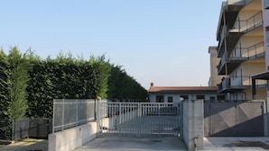 A gated entrance to a residential building with a clear sky and a hedge in the foreground.