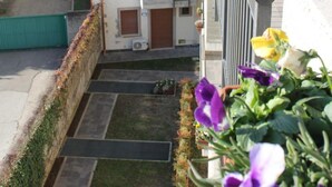 A multi-story building with balconies, a parking area, and a green space with flowers.