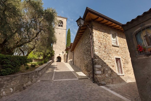 A narrow stone pathway leading to a tower with a bell. - Barchi Resort Apartments Suites Villa Castello - Loft Villa Castello (San Felice del Benaco)