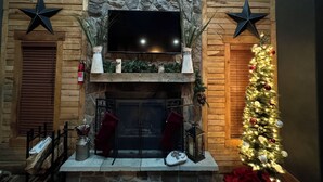A fireplace with a stone wall backdrop, a flat-screen TV mounted above, and a decorated Christmas tree to the right. - Hawks Ridge Cabin (Saint James)