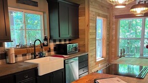 A modern kitchen with dark cabinets, a wooden island, and a large window providing a view of the outdoors. - Hawks Ridge Cabin (Saint James)