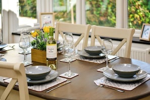 Una mesa de comedor dispuesta con platos, tazones y copas de vino, junto con una botella de vino y un centro de mesa floral.