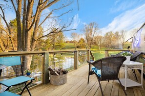 Une terrasse en bois avec des chaises et une table en osier, donnant sur un terrain de golf et un plan d’eau.