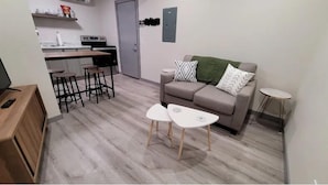 Un espace de vie compact comprenant un coin cuisine, un canapé agrémenté de coussins à motifs et deux petites tables.