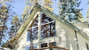 A two-story cabin with large windows, a balcony, and a chimney.