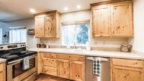 A kitchen with wooden cabinets, stainless steel appliances, and a window with a view of trees.