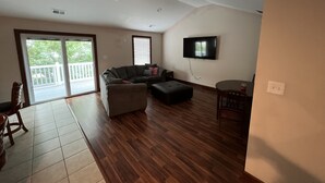 A spacious living room with a large sectional sofa, a small ottoman, a flat-screen TV mounted on the wall, and a sliding glass door leading to a balcony. - Luxury Beach Side Home 2 Bedroom Home by RedAwning (Norfolk)