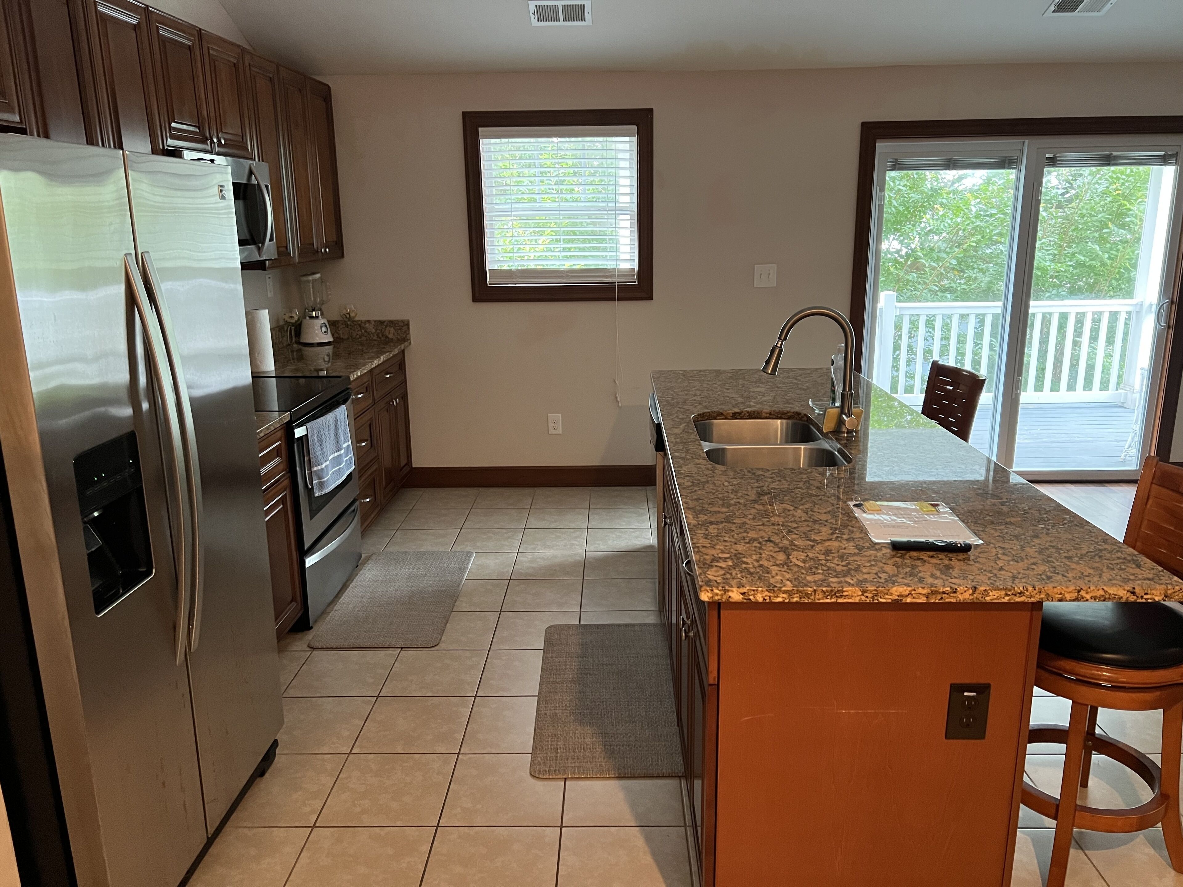 A kitchen with a stainless steel refrigerator, a built-in oven, a granite countertop, a sink, and a window with blinds.