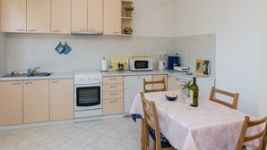 Une cuisine compacte avec des meubles de couleur claire, une cuisinière, un four à micro-ondes et un coin repas avec une table dressée pour deux personnes.
