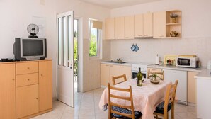 Une cuisine compacte avec un coin repas, des meubles en bois, un four à micro-ondes, un petit réfrigérateur et un téléviseur posé sur un meuble.