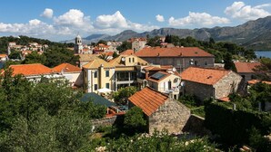 Une ville côtière à l’architecture traditionnelle, avec des bâtiments en pierre et des toits couverts de tuiles rouges, le tout se dressant sur un fond de montagnes et sous un ciel dégagé.