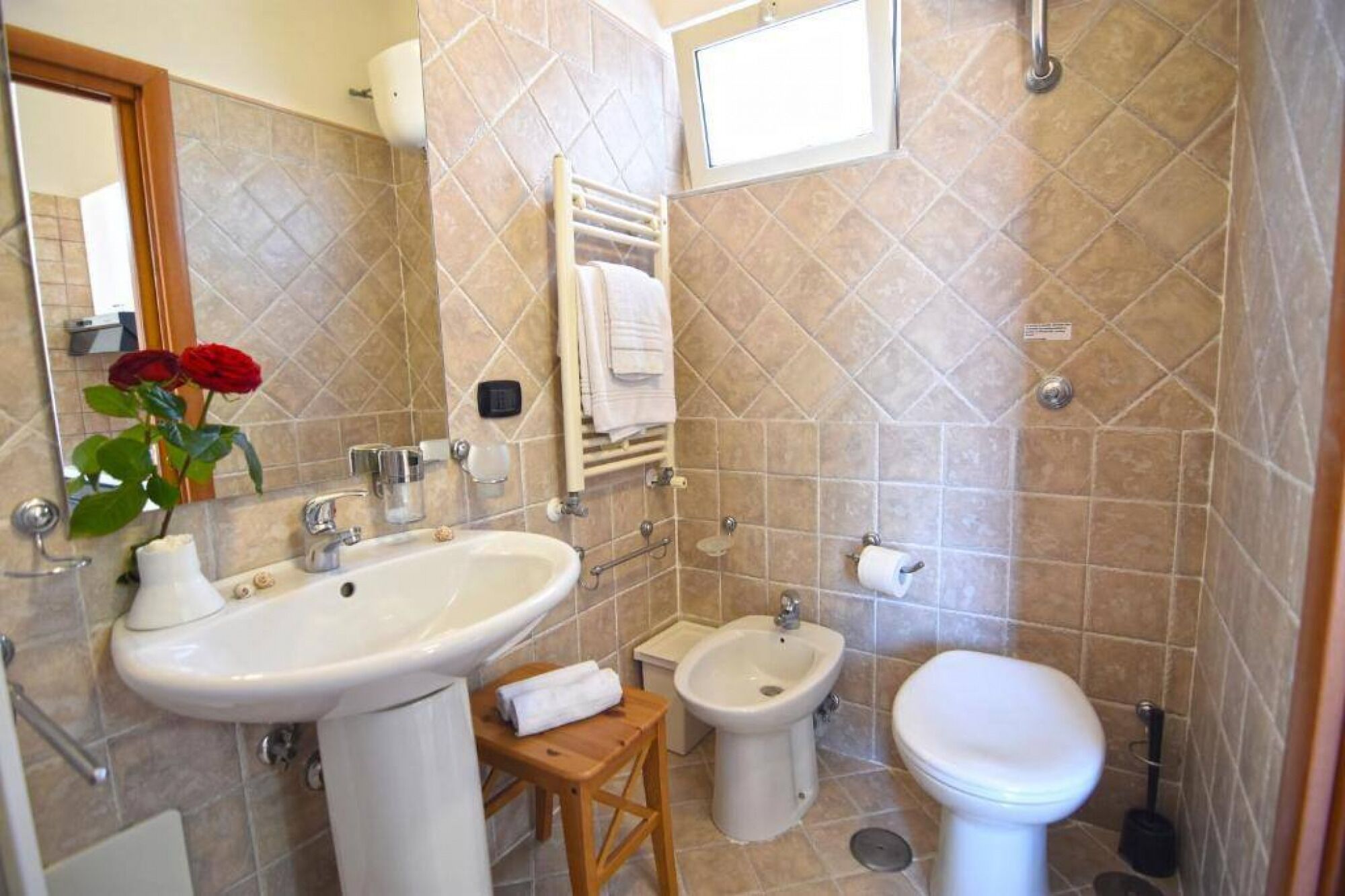 A bathroom with a sink, bidet, toilet, and a small wooden stool.
