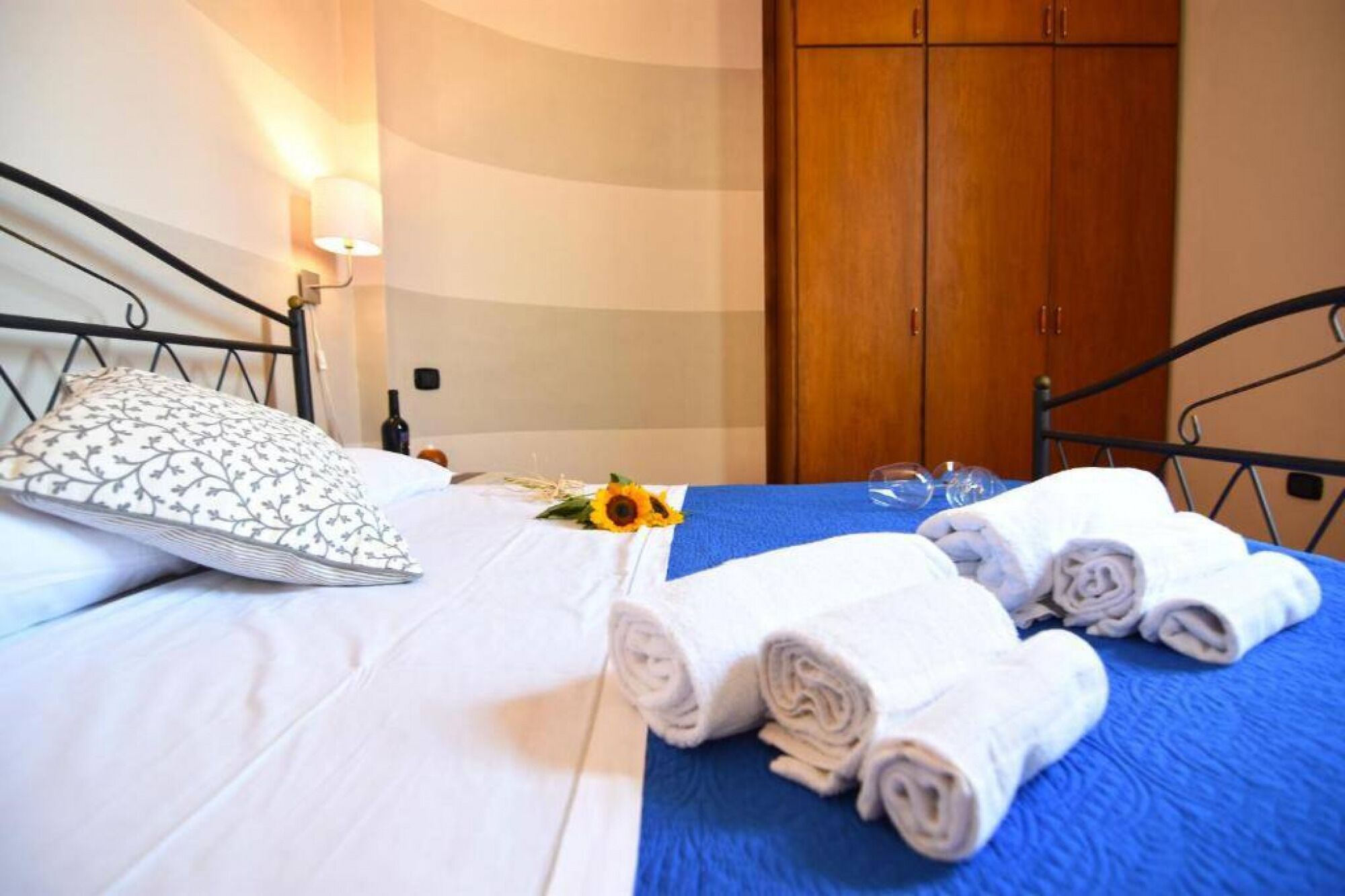 Cama bem arrumada com travesseiro estampado, manta azul e toalhas dobradas.