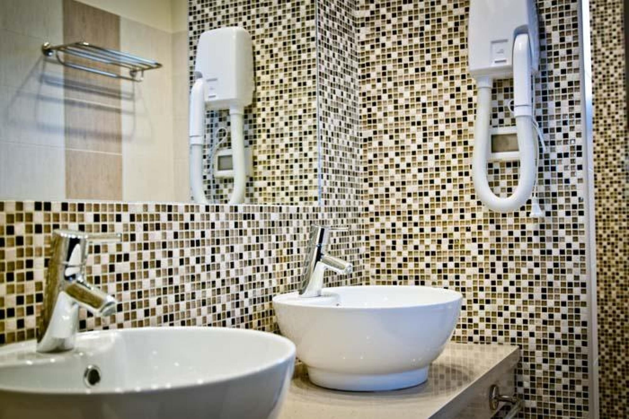 Uma casa de banho com duas pias, painel de azulejos e um porta-toalhas.