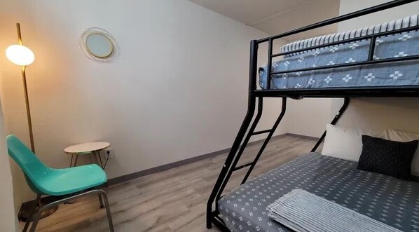 A bunk bed with a patterned bedspread, a teal chair, a small round table, and a wall-mounted light fixture. - Bighorn Loft in Downtown Custer, Sleeps 6 (Custer)