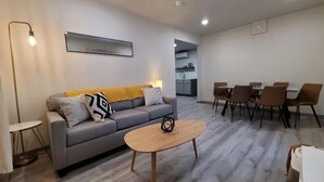 A modern living room with a grey sofa, a wooden coffee table, and a dining area with brown chairs and a white table.