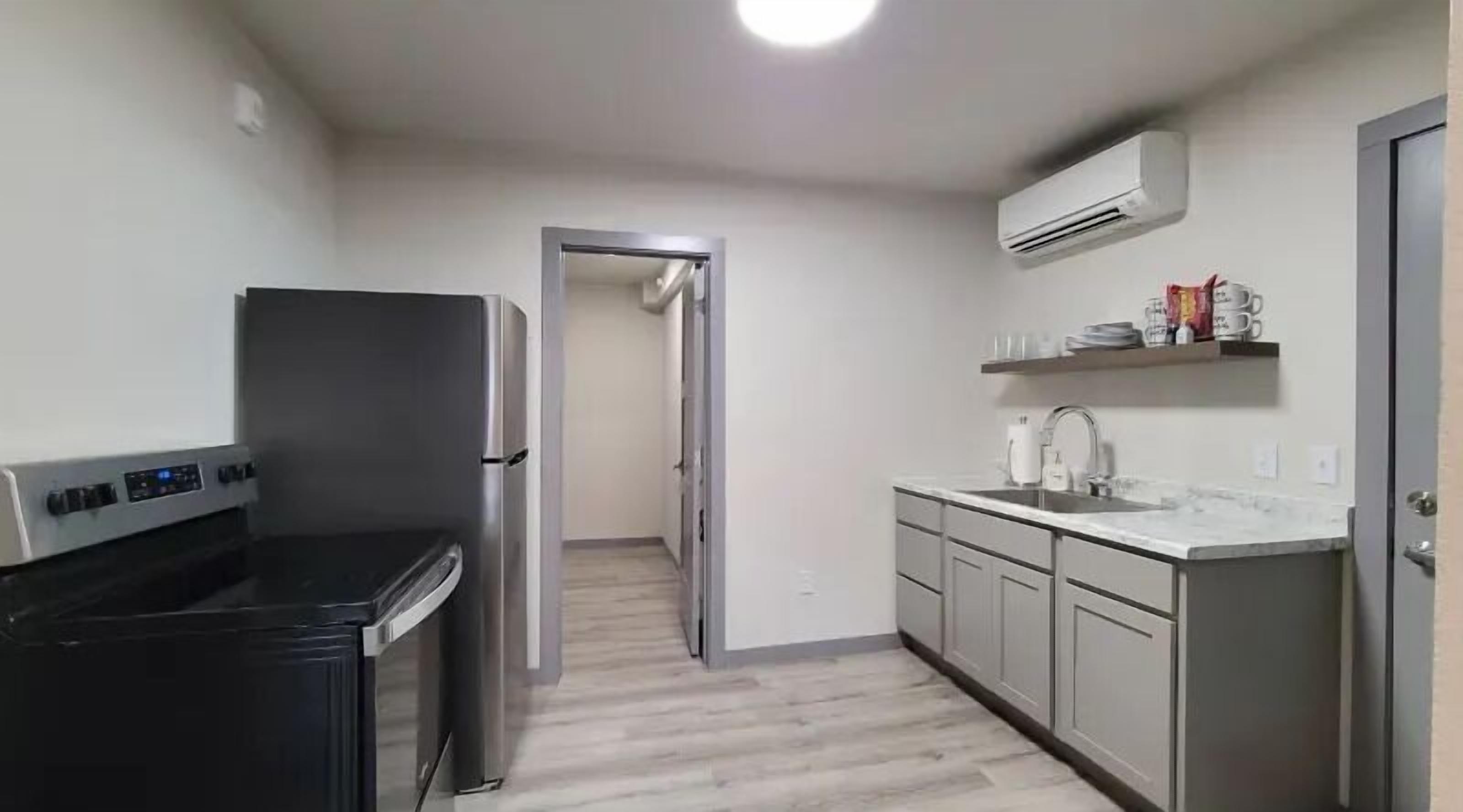 A compact kitchen with a built-in stove, a refrigerator, and a sink. There is a door leading to another room.