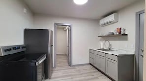 A compact kitchen with a built-in stove, a refrigerator, and a sink. There is a door leading to another room.