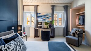 A modern bedroom with a bed, a side table, a chair, a small table with a plant, and a view of the outside through large windows. - Casa San lio - Casa San Lio (Noto)
