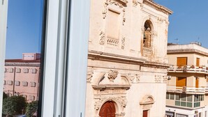 A window with a view of a historic building with ornate architecture, a clear blue sky, and a magazine on the windowsill. - Casa San lio - Casa San Lio (Noto)