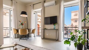 A modern living room with a dining area, a TV mounted on the wall, and a balcony with a view of the city. - Casa San lio - Casa San Lio (Noto)