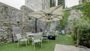 An outdoor seating area with stone walls, a table with chairs, and a large umbrella. - Barchi Resort Apartments Suites Villa Castello - Panoramic Villa Castello (San Felice del Benaco)