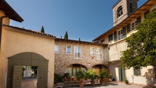 A courtyard with a stone building, a wooden door, and potted plants. - Barchi Resort Apartments Suites Villa Castello - Panoramic Villa Castello (San Felice del Benaco)