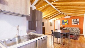 A modern kitchen with a sink and cabinets, a dining area with a table and chairs, and a living room with a sofa and a rug. - Barchi Resort Apartments Suites Villa Castello - Panoramic Villa Castello (San Felice del Benaco)