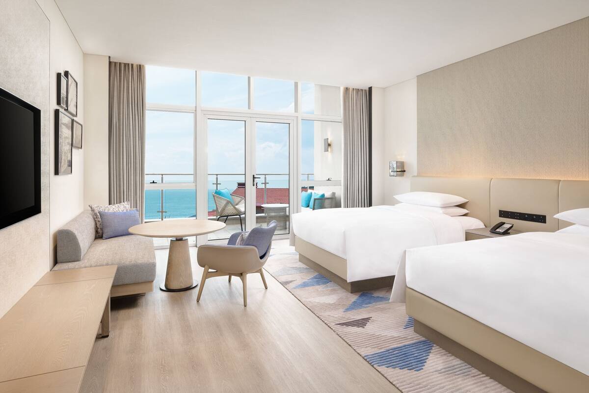 A hotel room with a large window, a sofa, a bed, a desk, and a chair.