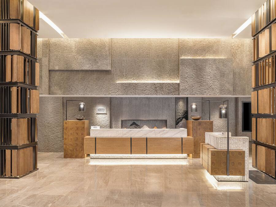 A modern hotel room with a large bed, a wooden sideboard, and a textured wall.