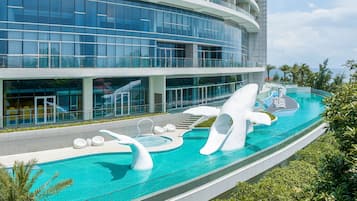 Experience the unique architecture and serene atmosphere of this hotel, featuring a spacious pool area with a dolphin-shaped slide and hot tub surrounded by lush greenery.